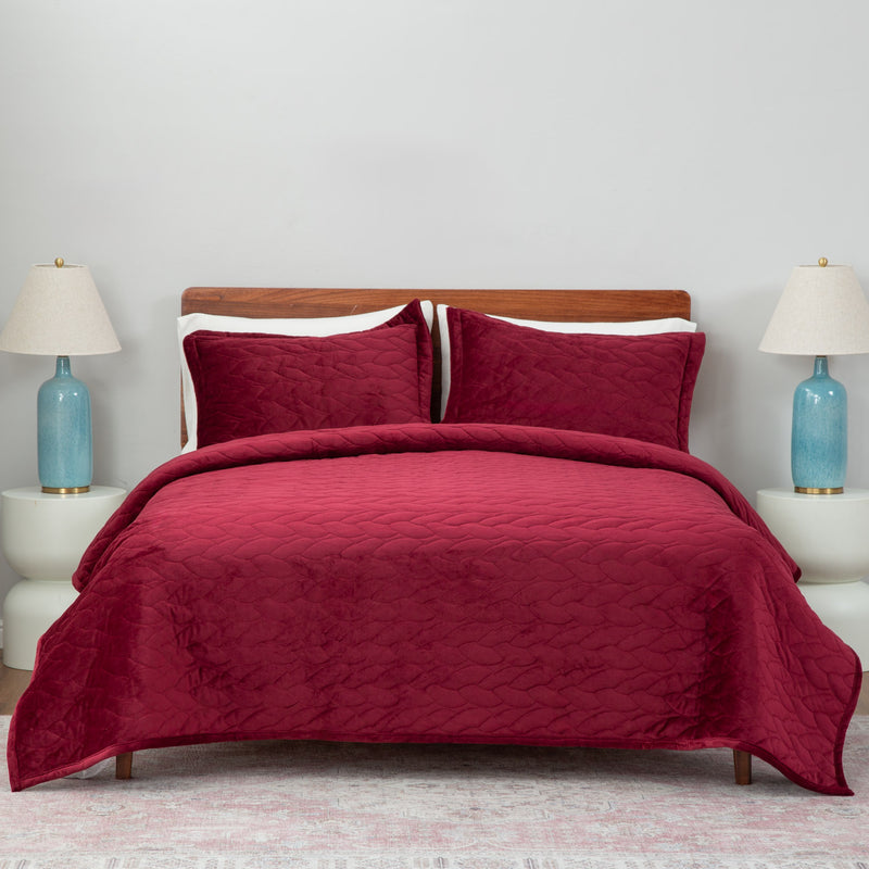 Red quilt set decorated on a bed in a neutral bedroom.