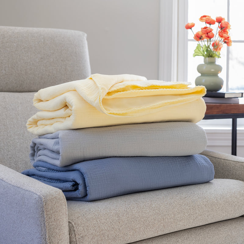 A stack of a yellow, grey, and blue gauze throws folded neatly on a grey chair.
