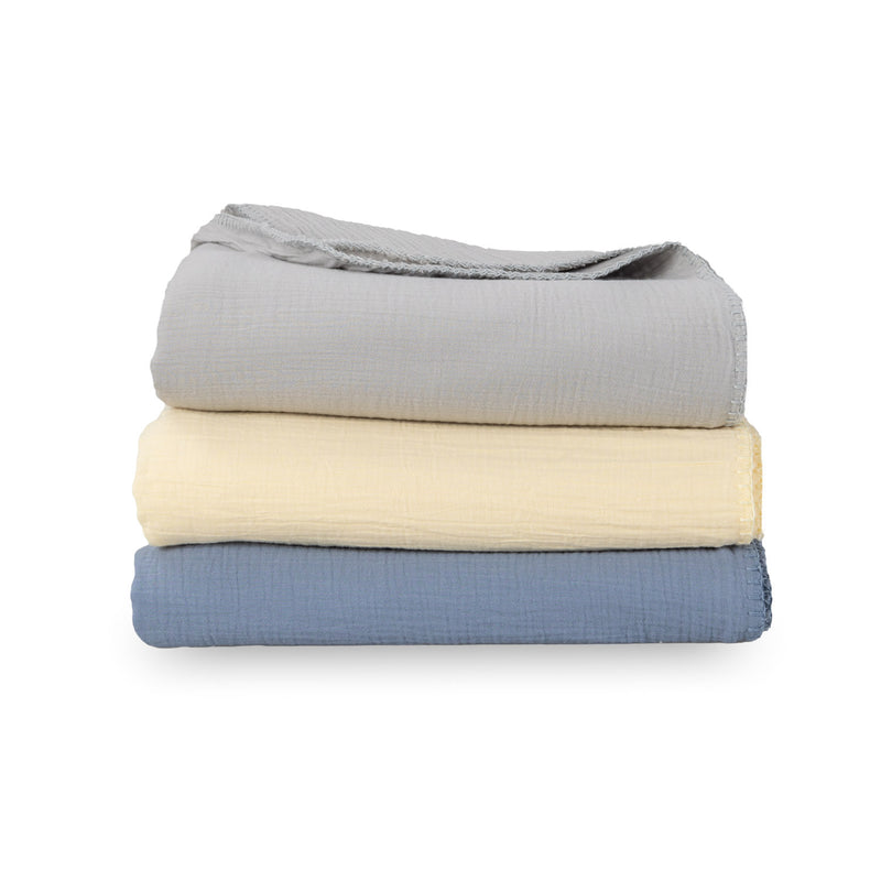 Grey, yellow, and blue VelvetLoft Gauze Throws stacked neatly on a white surface.