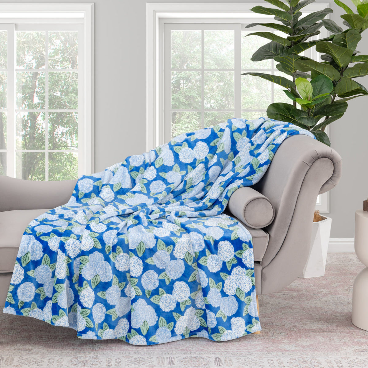 Krissy Mast Artist Series printed hydrangea print throw draped neatly over a grey sofa in a staged room.