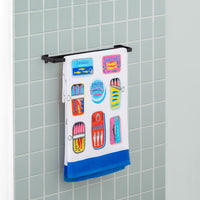 Bex Morley Sardine Tin beach towel draped neatly over a metal towel rod in a bathroom.