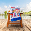 A stack of 3 printed beach towels stacked on top of a wooden chair by a pond.