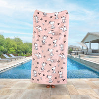 A person holding up a pink Peanuts beach towel while standing by a pool.