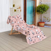 A pink Peanuts beach towel laid on a wooden lounge chair on a patio.