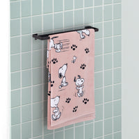 A pink Peanuts beach towel folded over a metal rod in a bathroom.