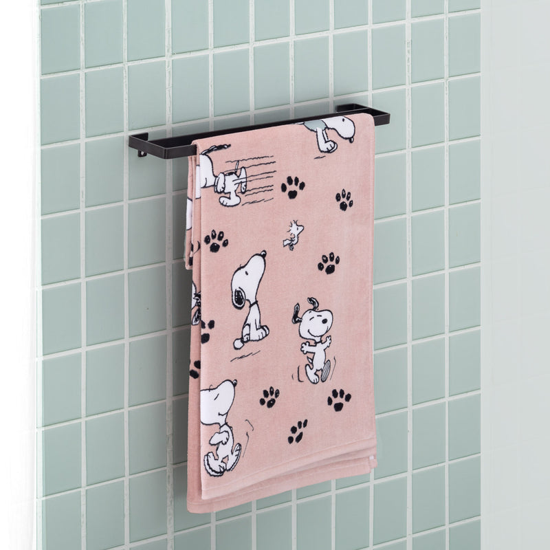 A pink Peanuts beach towel folded over a metal rod in a bathroom.