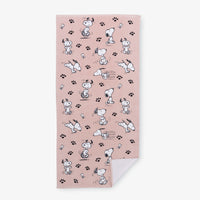 A pink Peanuts beach towel laid flat on a white surface.