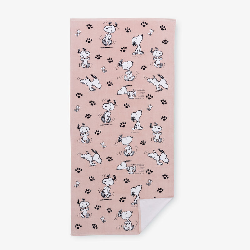 A pink Peanuts beach towel laid flat on a white surface.