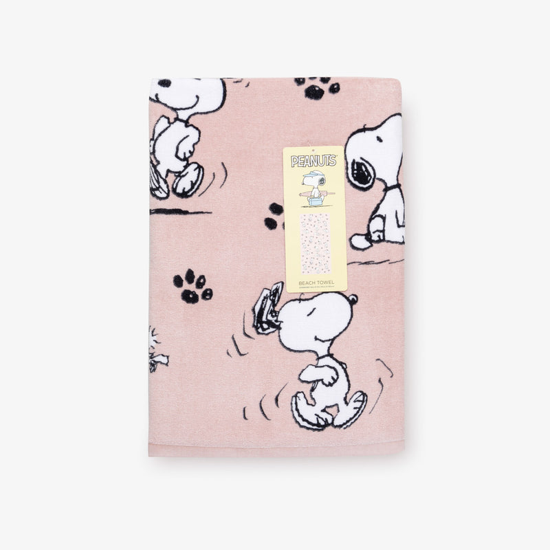 A pink Peanuts beach towel folded neatly on a white surface.