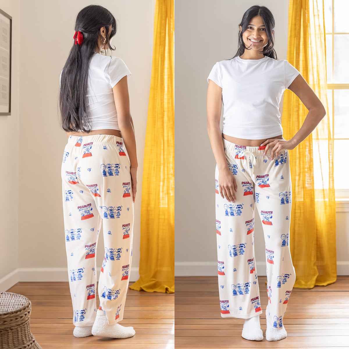 A woman wearing cream Peanuts printed lounge pants while standing in a living room.