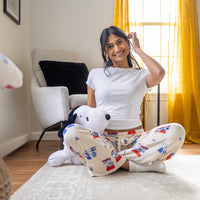 A woman sitting down on a rug wearing peanuts snoopy lounge pants.