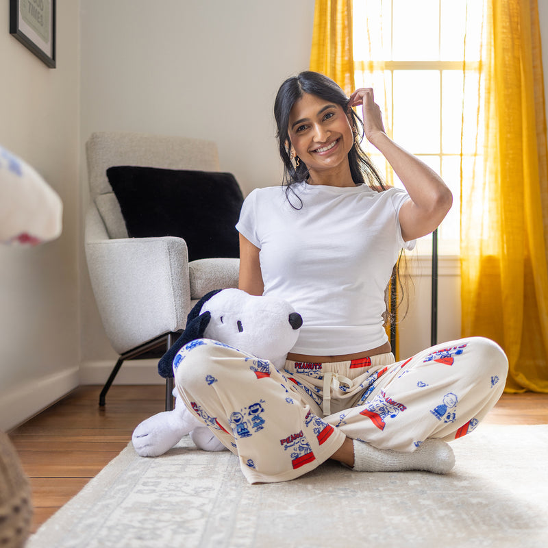 A woman sitting down on a rug wearing peanuts snoopy lounge pants.
