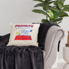 Peanuts Social Club Pillow sitting ona black blanket on a grey couch in a staged room.