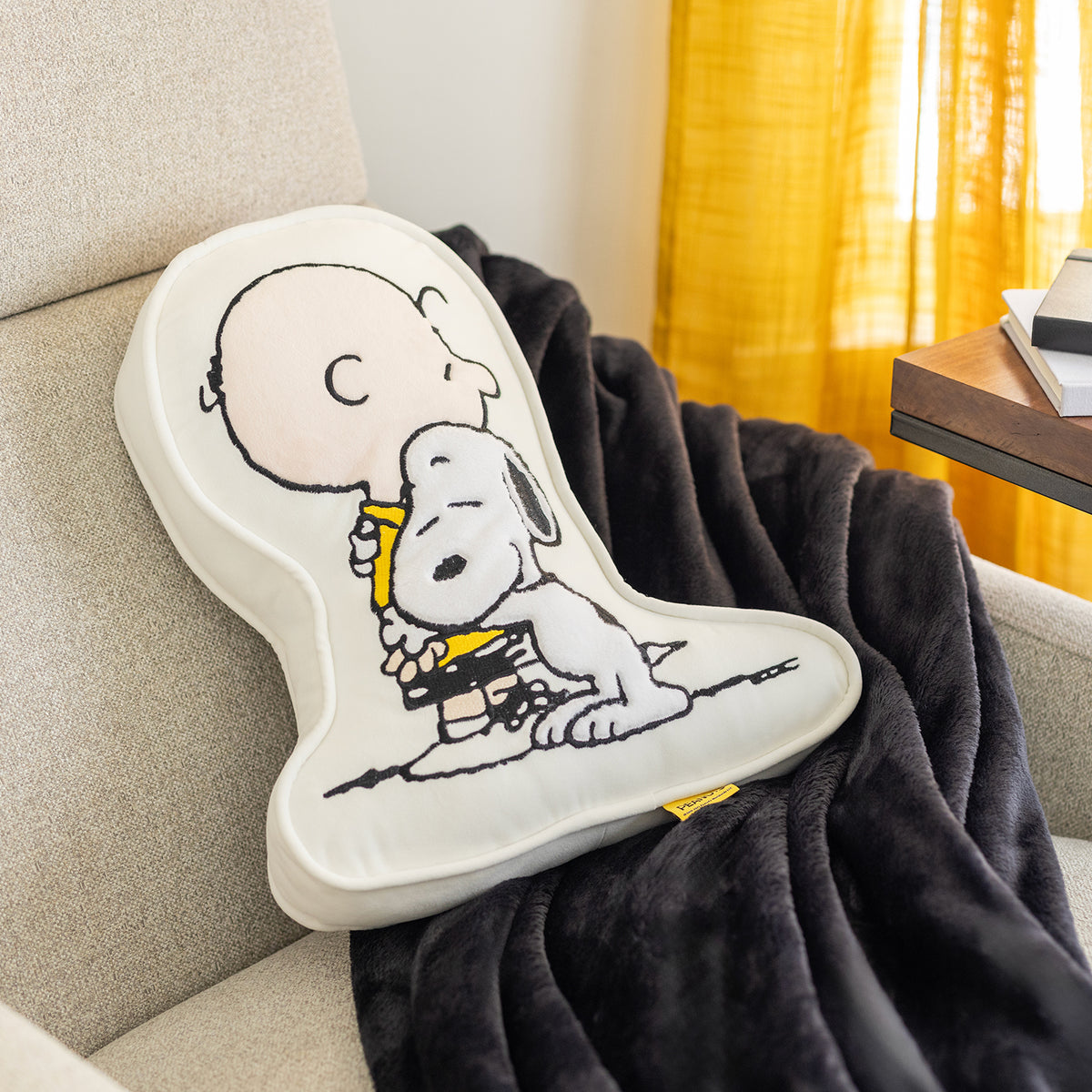 Charlie Brown & Snoopy embroidered pillow laying on a plush black throw on a chair.
