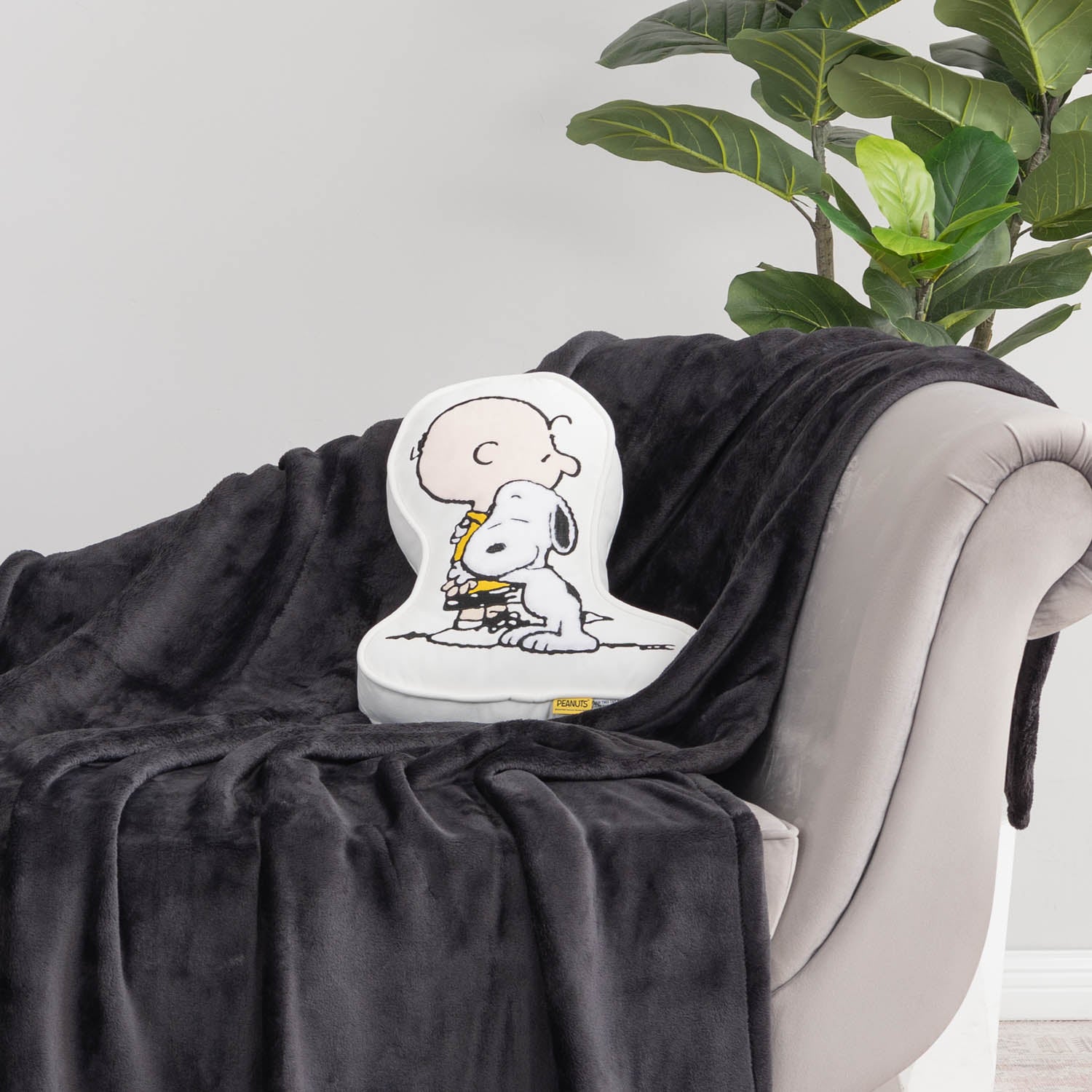 Charlie Brown & Snoopy embroidered pillow sitting on a black throw on a grey chair.