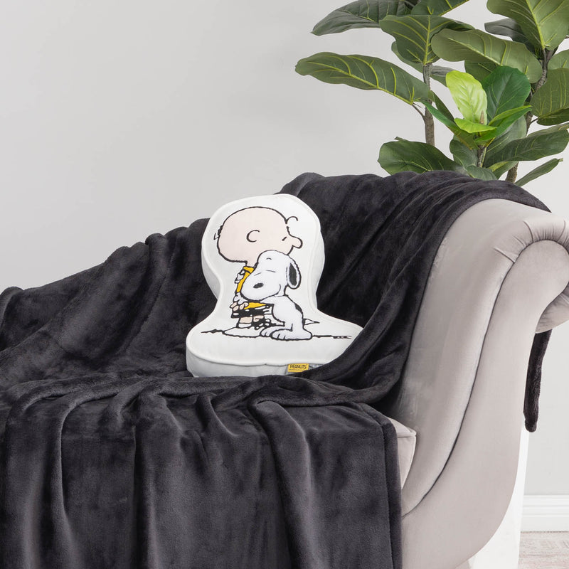 Charlie Brown & Snoopy embroidered pillow sitting on a black throw on a grey chair.
