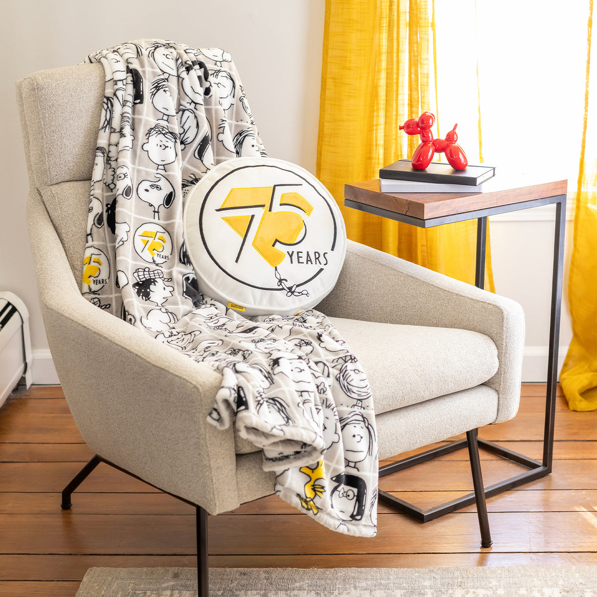 Peanuts 75th Anniversary Throw and Pillow on a beige chair.