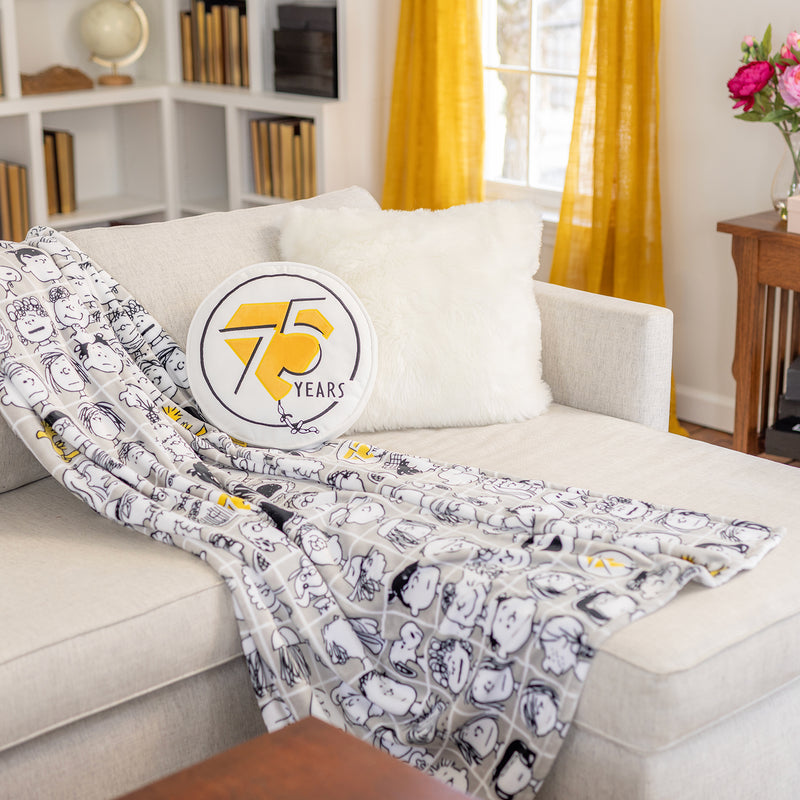 Peanuts 75th Anniversary Throw and Pillow on a beige sofa.