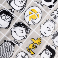 Close up of a Peanuts 75th Anniversary Throw & Pillow Set draped over a brown leather chair.