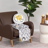 Peanuts 75th Anniversary Throw & Pillow Set draped over a brown leather chair.