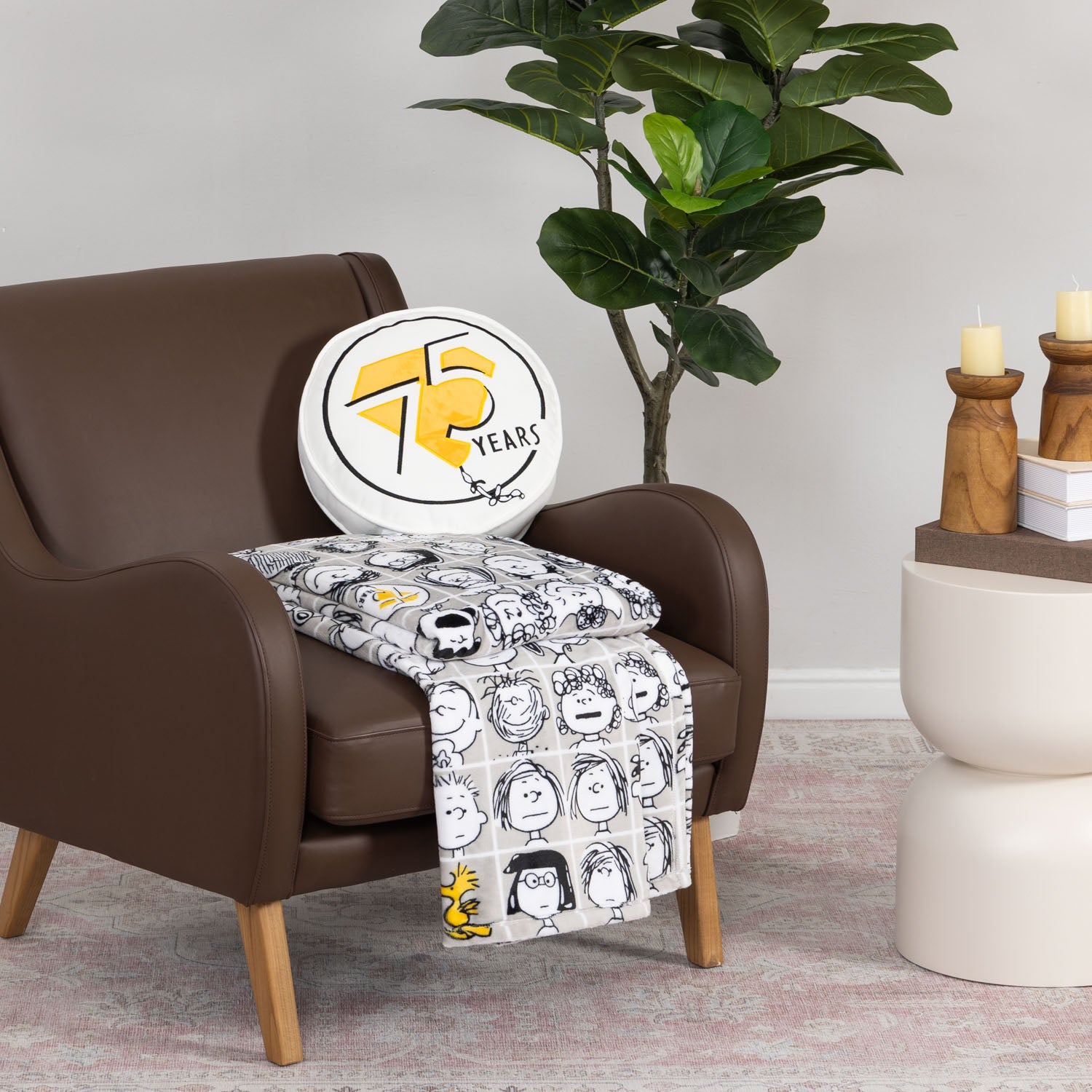 Peanuts 75th Anniversary Throw & Pillow Set draped over a brown leather chair.