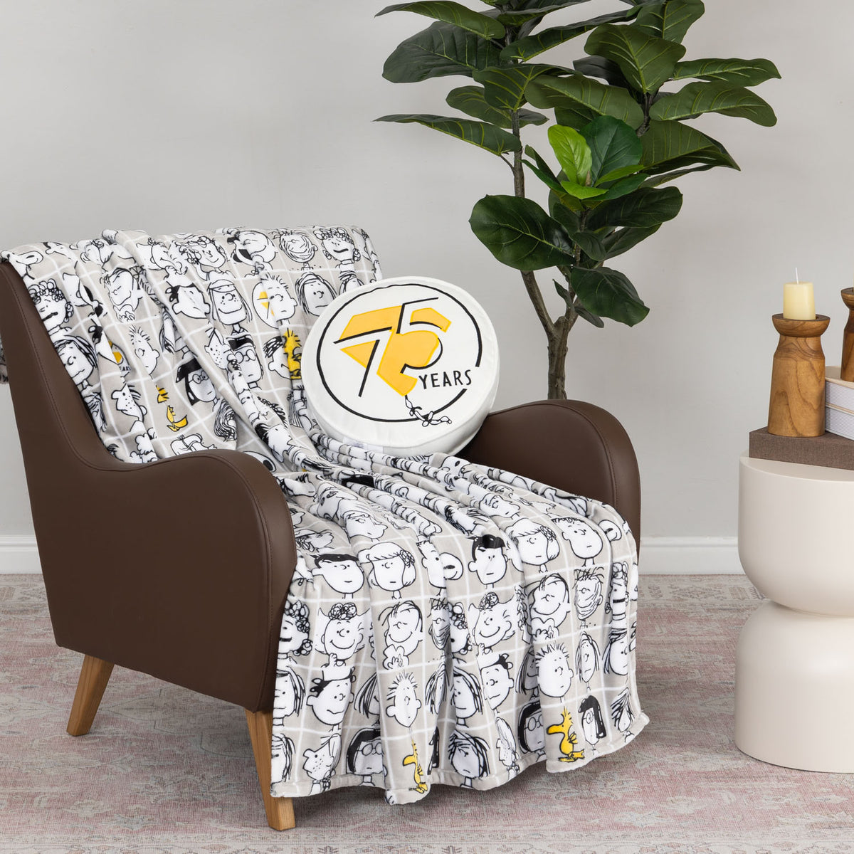Peanuts 75th Anniversary Throw & Pillow Set draped over a brown leather chair.