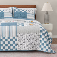 Bed with blue and white checkered and patterned comforter, pillows, and lamp in a room.