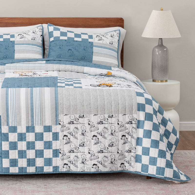 Bed with blue and white checkered and patterned comforter, pillows, and lamp in a room.