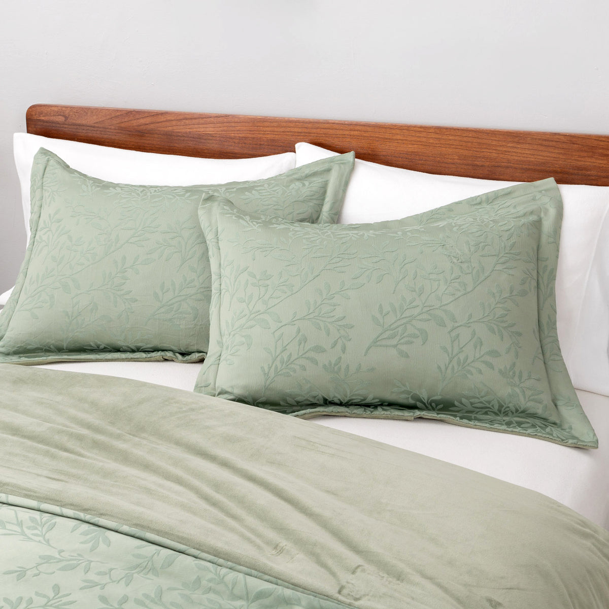 Green patterned pillows on a bed with a wooden headboard.