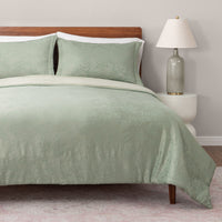 Green textured bedding set on a bed with a wooden headboard and lamp.