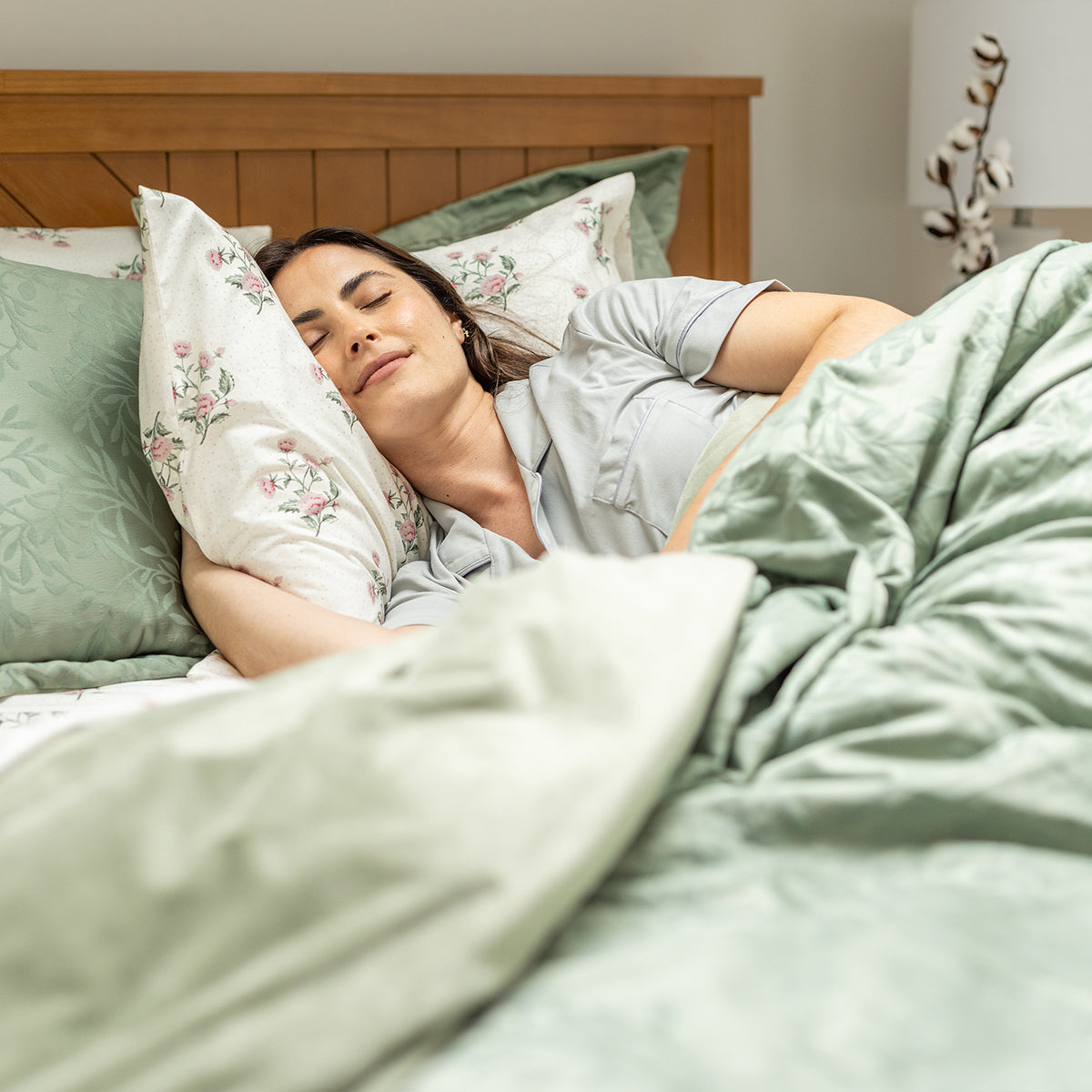 Woman sleeping peacefully in a bed with light green bedding and floral pillows.
