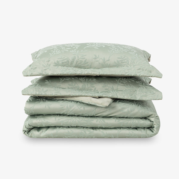 Folded green comforter set with pillows on a white background
