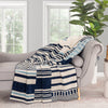 Striped blanket draped over a gray armchair in a room with large windows and a plant.