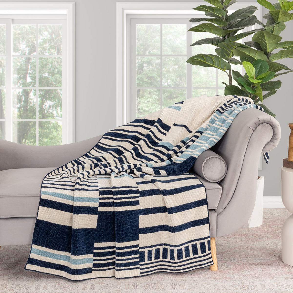 Striped blanket draped over a gray armchair in a room with large windows and a plant.