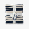 Navy and white striped blanket with a white ribbon and tag on a light gray background