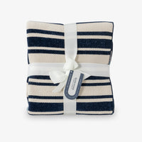 Navy and white striped blanket with a white ribbon and tag on a light gray background