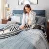 Woman arranging striped blanket on a bed in a bedroom setting