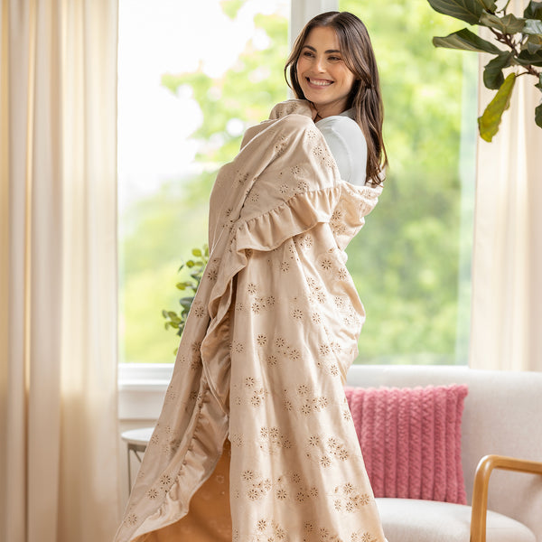 Woman wearing a beige floral throw in a bright room with a couch and plant.