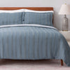 Blue striped bedding set on a bed with a wooden headboard and lamp in the background.