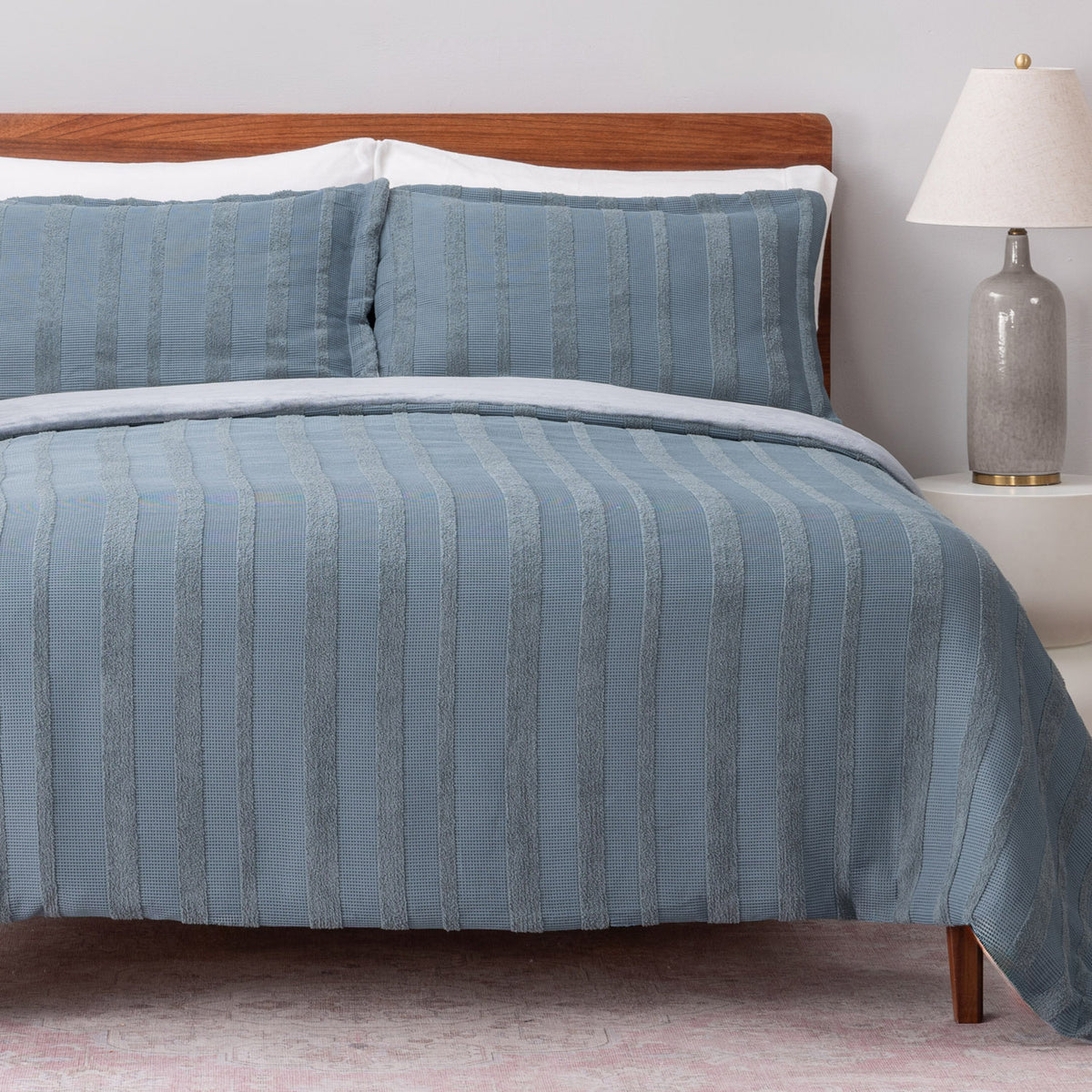 Blue striped bedding set on a bed with a wooden headboard and lamp in the background.