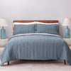 Blue striped bedding set on a bed with matching pillows and lamps in the background.