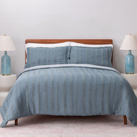Blue striped bedding set on a bed with matching pillows and lamps in the background.