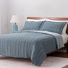 Blue striped bedding set on a bed with a wooden headboard and lamp in the background.