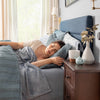 Woman sleeping in a bedroom with a blue headboard and wooden nightstand.