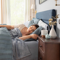 Woman sleeping in a bedroom with a blue headboard and wooden nightstand.