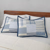 Pair of blue and white stripe quilted pillows on a bed with a wooden headboard.