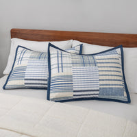 Pair of blue and white stripe quilted pillows on a bed with a wooden headboard.