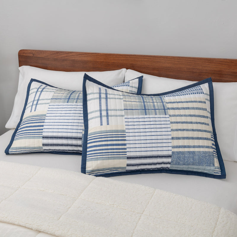 Pair of blue and white stripe quilted pillows on a bed with a wooden headboard.