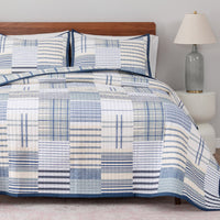 Bed with blue and white checkered comforter and pillows, nightstand with lamp in the background.