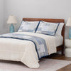 Bed with blue and white patterned Quilt on top of white bedding in a bedroom setting
